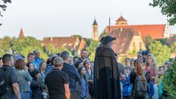Ein Nachtwächter steht vor einem Publikum vor der Stadt Rothenburg ob der Tauber.  | Bild:Rothenburg Tourismus Service/Pfitzinger