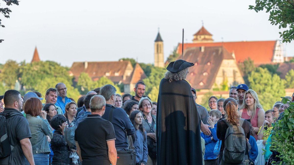 Ein Nachtwächter steht vor einem Publikum vor der Stadt Rothenburg ob der Tauber. 