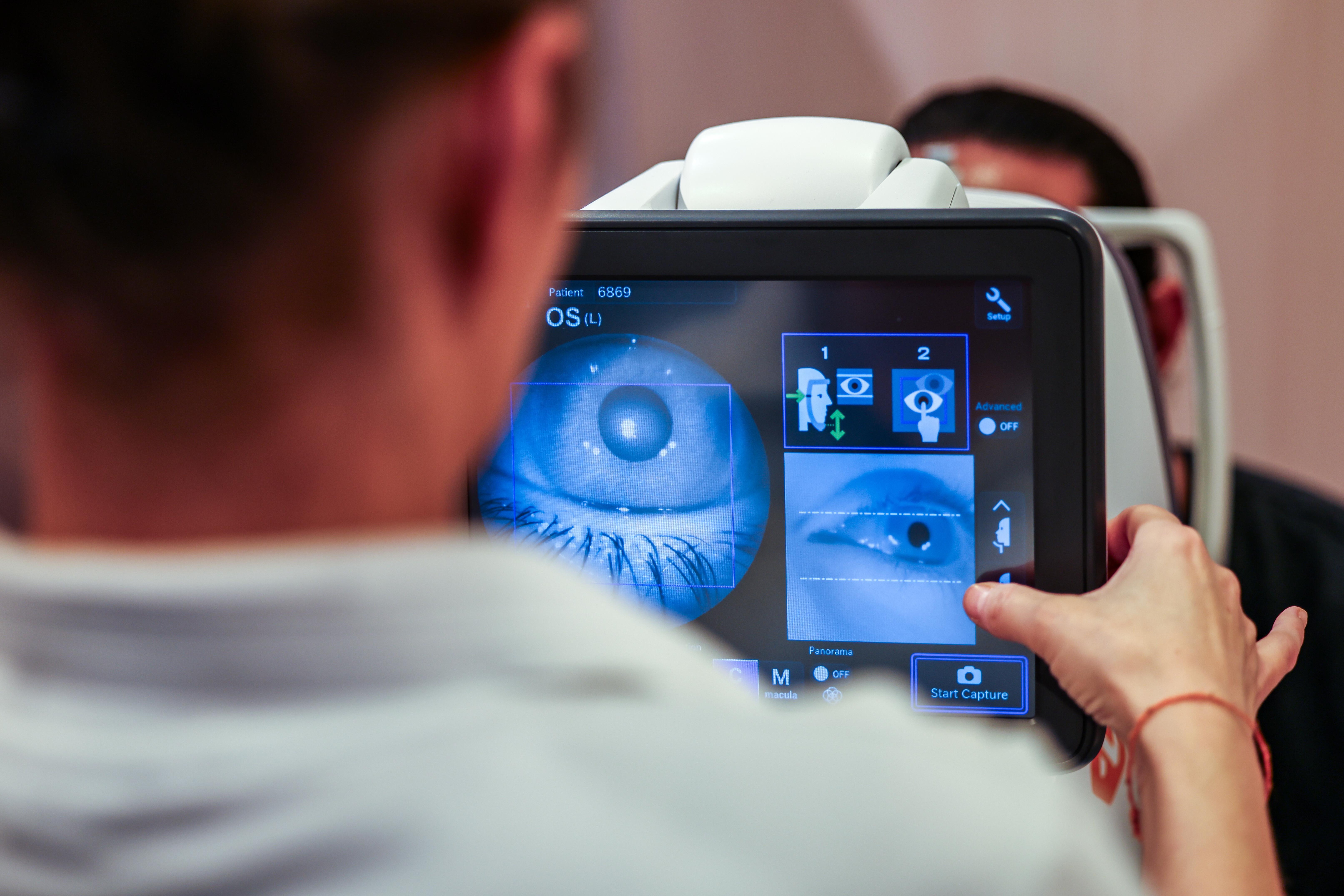 Auf einem Monitor sieht eine dm-Verkäuferin bei einem Augenscreening das Auge eines Kunden.