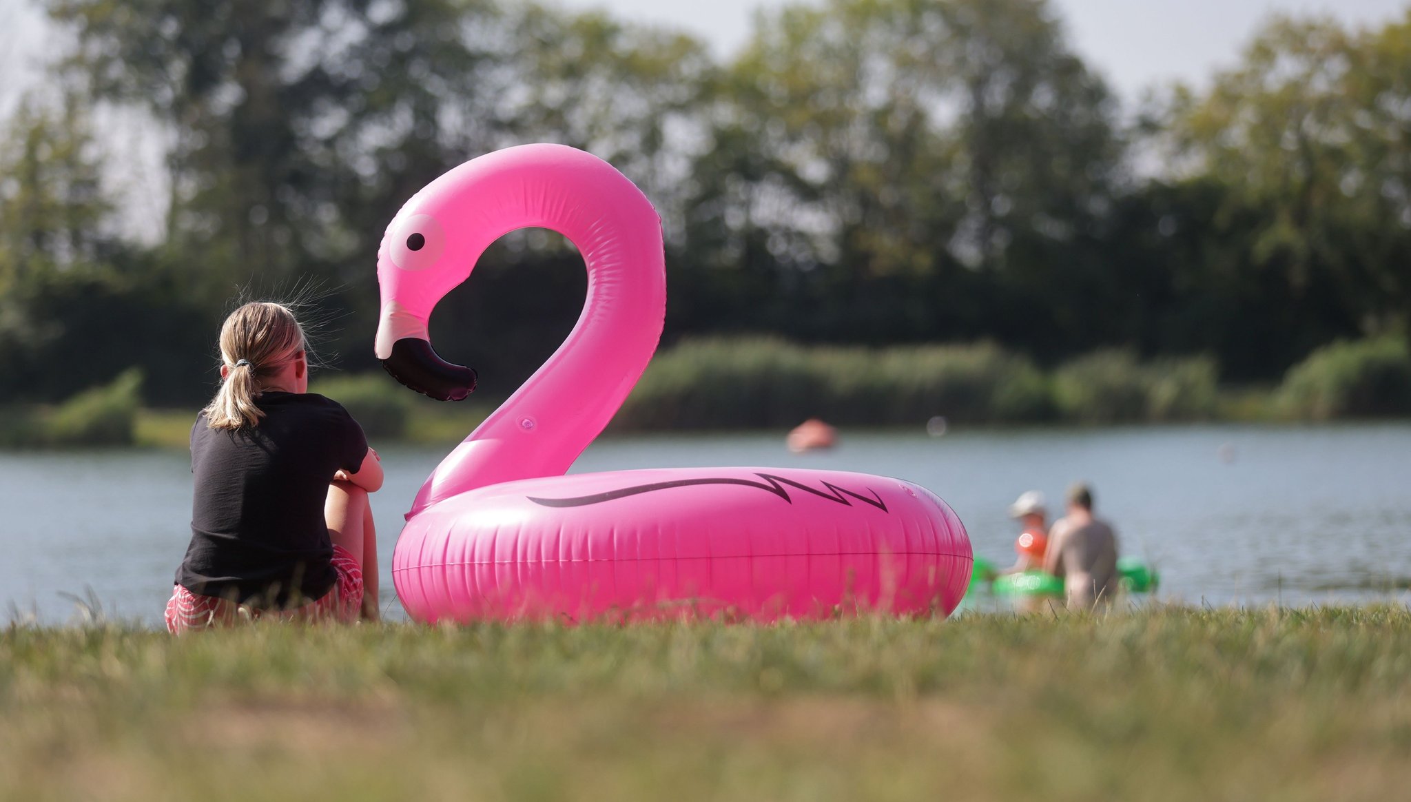 Ein Mädchen sitzt neben einem überdimensionalen Schwimmring in Form eines Flamingos an einem Badesee. (Symbolbild)
