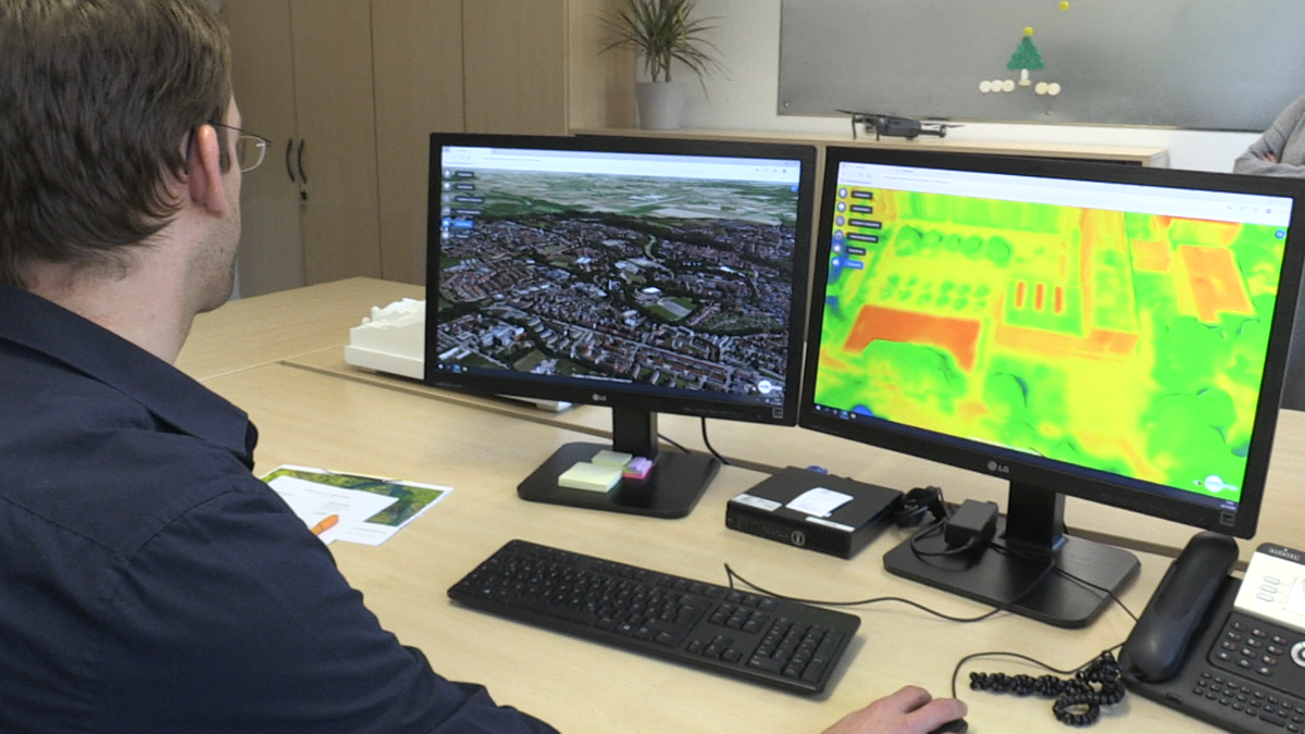 Der Landsberger Stadtplaner Daniel Broschart sitzt vor zwei Monitoren, einer zeigt den Digitalen Zwilling von Landsberg von oben, das andere zeigt die Wärmebildansicht mit roten, gelben und grünen Flächen.
