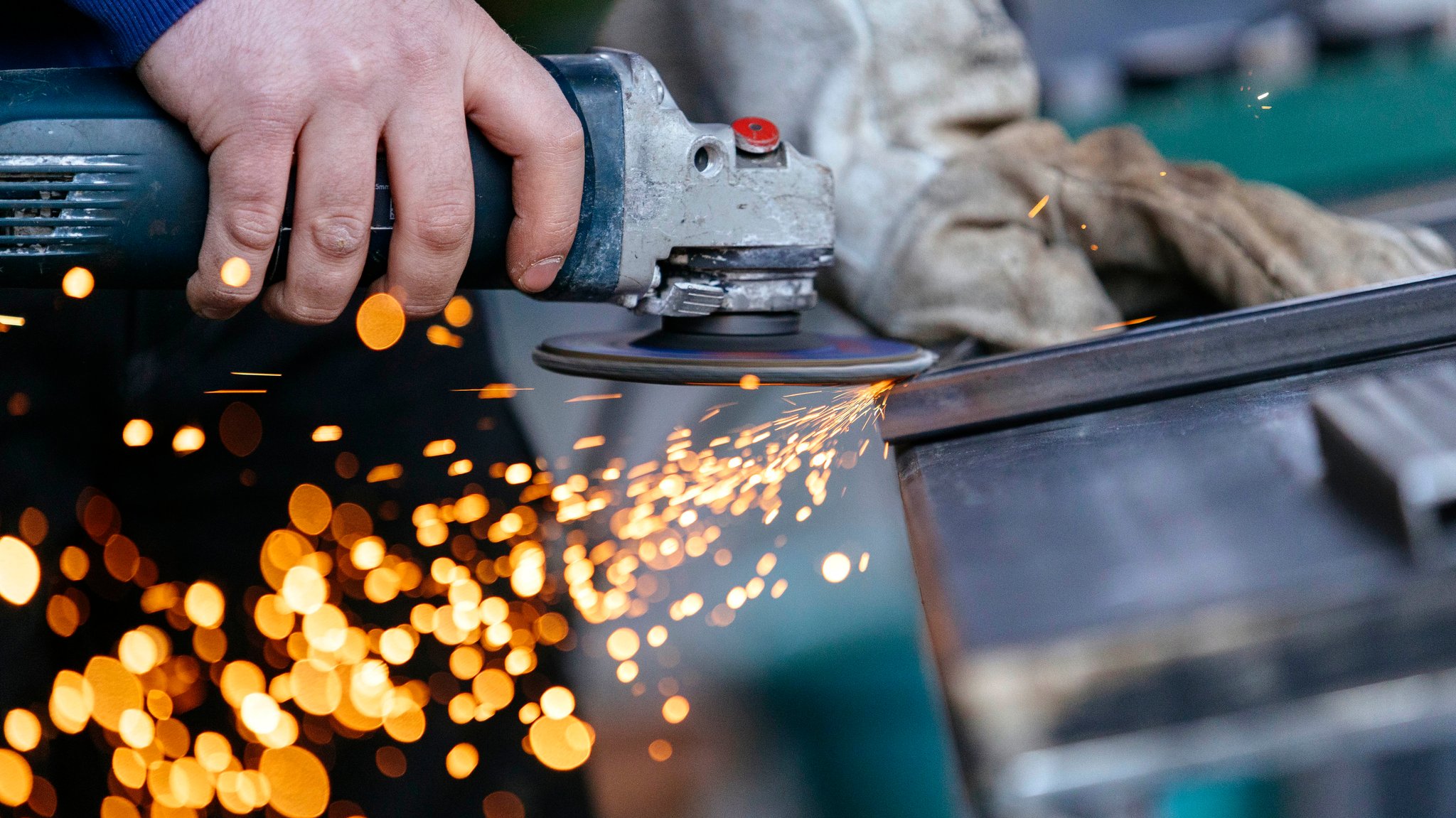 Ein Handwerker schleift Metall, Funken fliegen aus dem Bild.