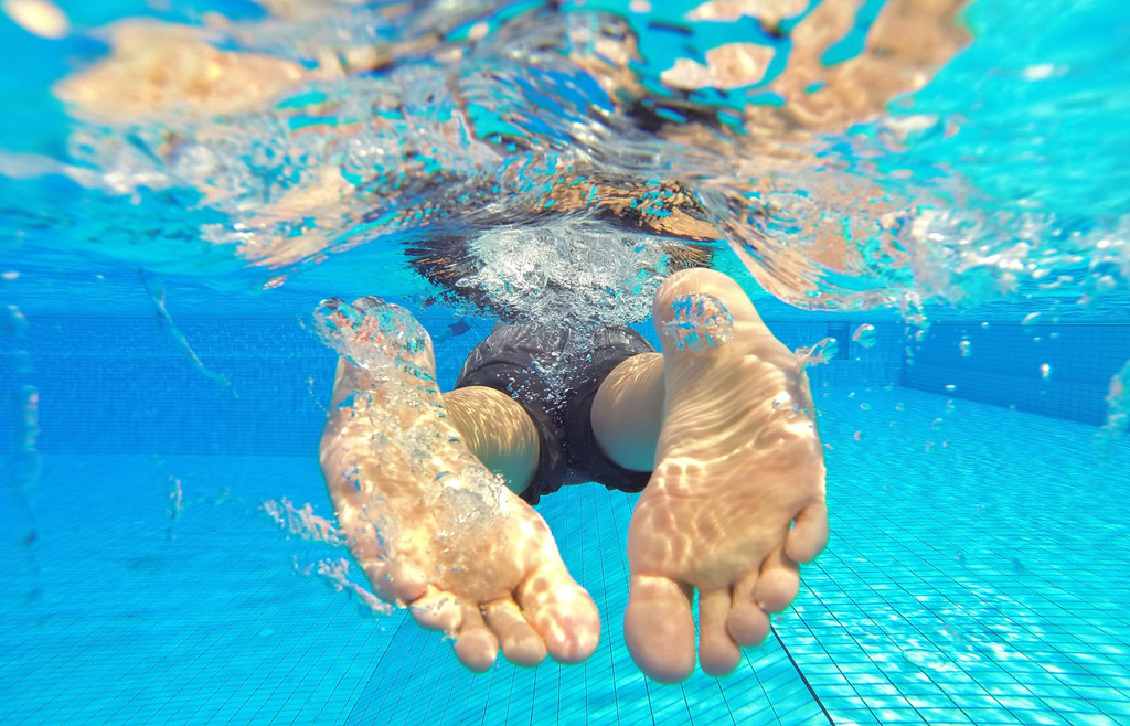 Ein Schwimmer im Schwimmbad von hinten. Im Wasser steigt der Harndruck beim Menschen.