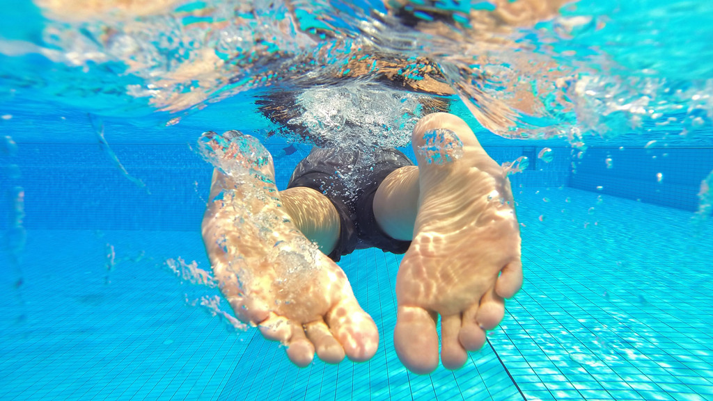 Ein Schwimmer im Schwimmbad von hinten. Im Wasser steigt der Harndruck beim Menschen.