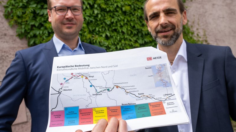Dieter Müller (l) und Matthias Neumaier (r) von der Deutschen Bahn halten nach einer Pressekonferenz einen Plan mit der Trasse für die Neubaustrecke des Brenner-Nordzulaufs in den Händen. (13.07.2022)