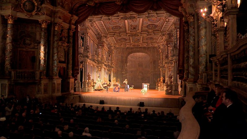 Blick auf eine Bühne eines Barocktheaters, auf der Künstler musizieren.