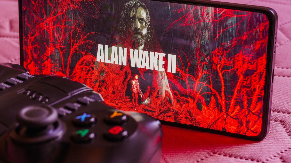 Smartphone mit Ausschnitt aus dem Spiel Alan Wake 2 und davor eine Spielekonsole.