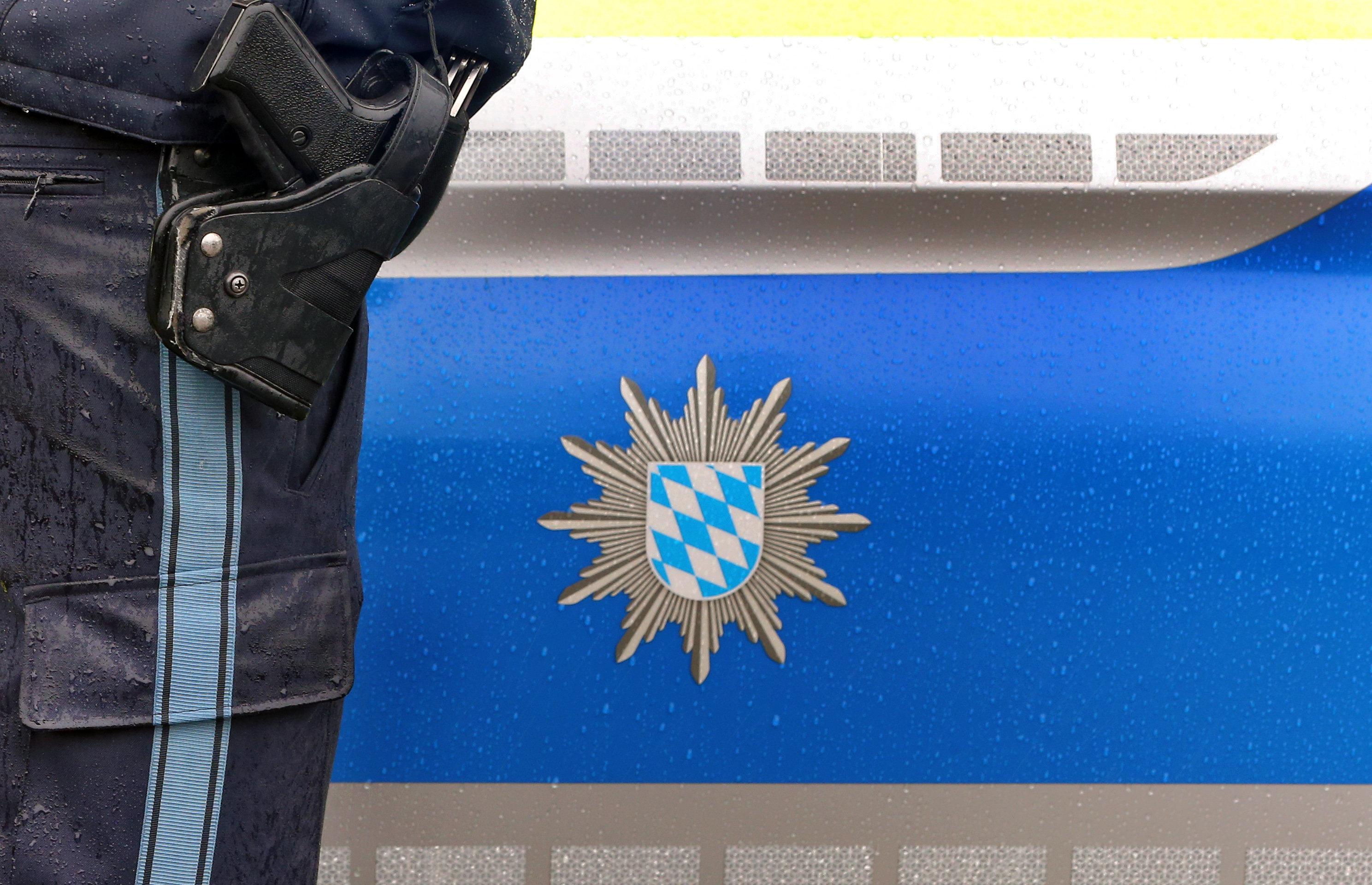 Ein Polizist mit Handschellen und einer Pistole am Gürtel steht vor einem Streifenwagen (Archiv- und Symbolbild)