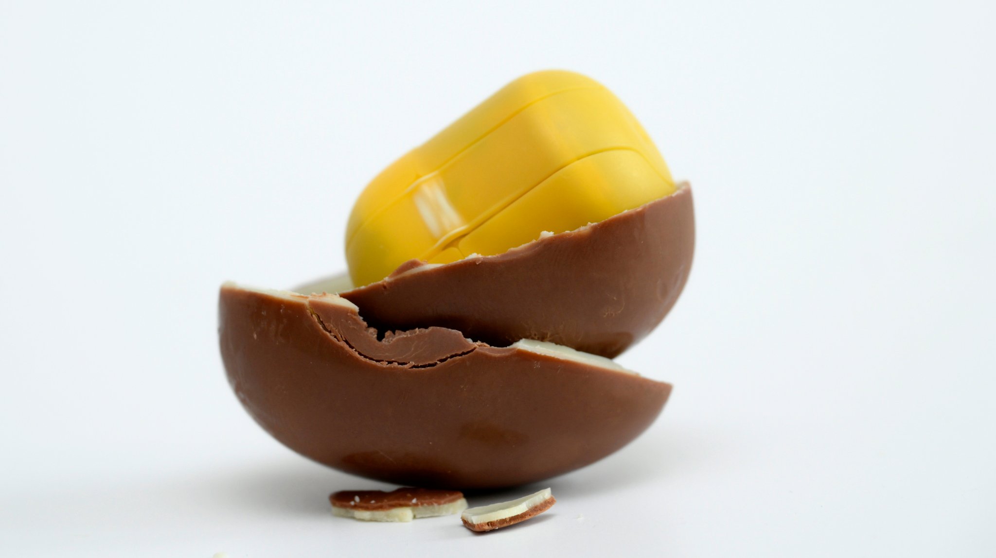 Das Bild zeigt ein geöffnetes Schokoladen-Überraschungsei mit gelbem Kunststoff-Innenbehälter auf weißem Hintergrund. Die Schokoladenhülle ist in mehrere Stücke zerbrochen, einige kleine Schokoladenstücke liegen davor. | Bild: picture alliance / M.i.S. | Bernd Feil Das Bild zeigt ein geöffnetes Schokoladen-Überraschungsei mit gelbem Kunststoff-Innenbehälter auf weißem Hintergrund. Die Schokoladenhülle ist in mehrere Stücke zerbrochen, einige kleine Schokoladenstücke liegen davor.