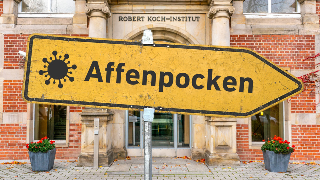 Symbolbild:  Ein gelbes, zerkratztes Hinweisschild mit einem Virus-Piktogramm und der Aufschrift "Affenpocken" vor dem Robert-Koch-Institut (RKI) am Nordufer in Berlin-Wedding.