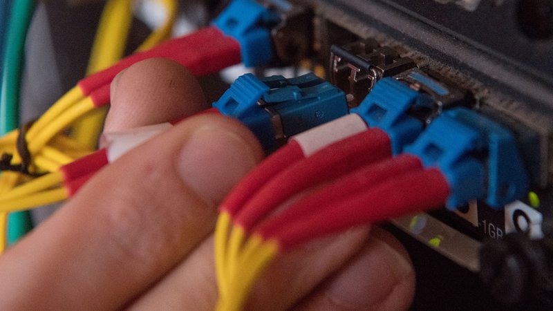 Ein Mann demonstriert, wie ein Glasfaserkabel in einen Router gesteckt wird. | Bild: picture alliance / Marijan Murat/dpa | Marijan Murat Ein Mann demonstriert, wie ein Glasfaserkabel in einen Router gesteckt wird.