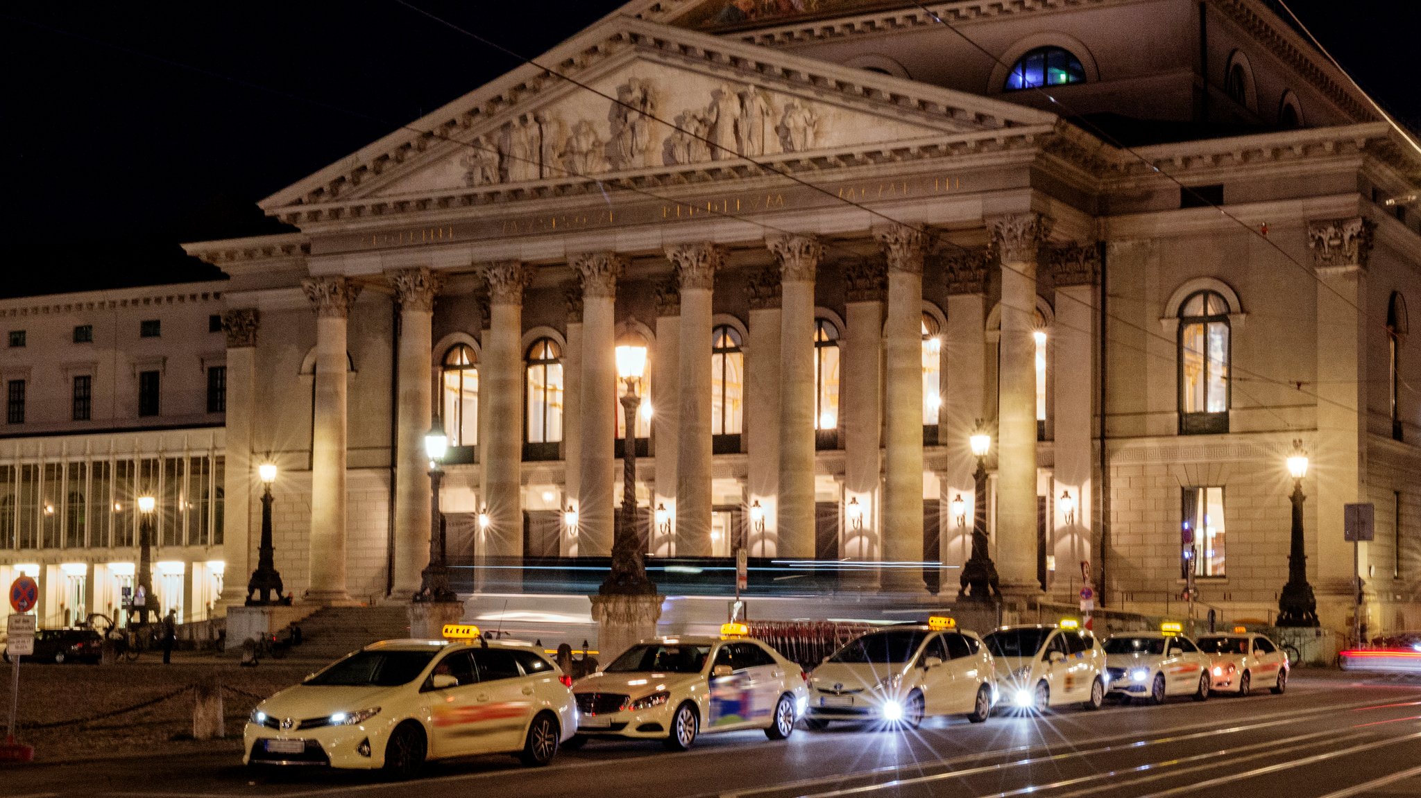 Das Residenz- und Nationaltheater am Max-Joseph-Platz in München mit Taxistand und Lichtstreifen eines Autos.