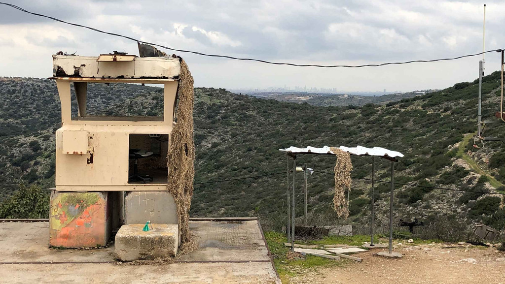 Ein militärisch aussehender Wachposten einer jüdischen Siedlung im grünen Westjordanland. Am Horizont sieht man die Hochhäuser einer größeren Stadt.