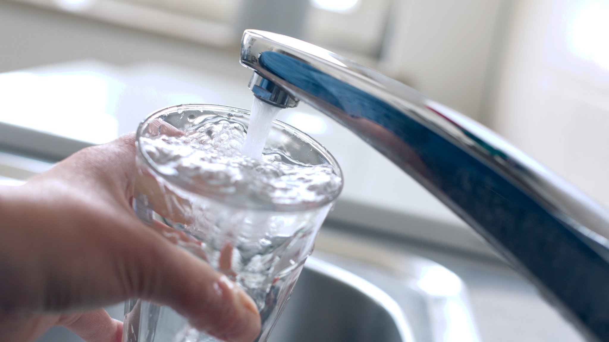 Jemand füllt am Wasserhahn ein Glas mit Leitungswasser.