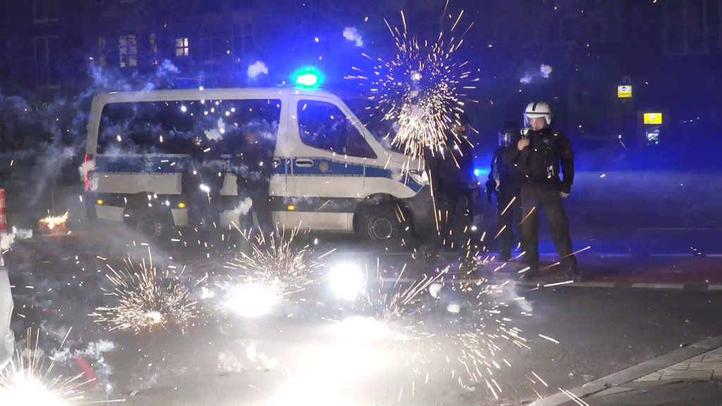  Polizeibeamte stehen hinter explodierendem Feuerwerk. (Symbolbild)