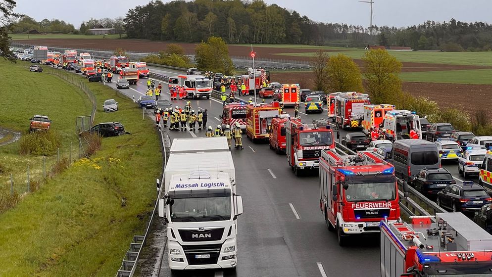 Zahlerreiche Rettungsfahrzeuge stehen auf einer Autobahn, neben der Fahrbahn liegen Autos auf einer Wiese.  | Bild:News5