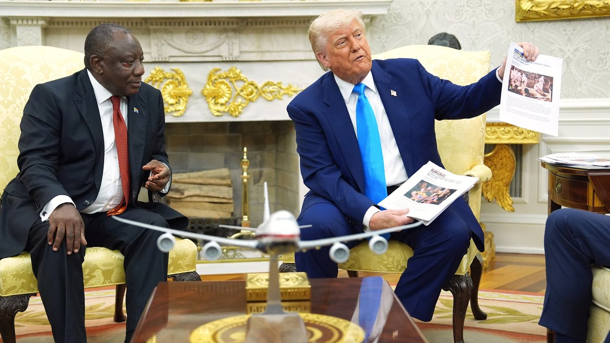 Zu sehen sind Südafrikas Präsident Cyril Ramaphosa und US-Präsident Donald Trump, die im Oval Office des Weißen Hauses nebeneinander sitzen. Donald Trump hält einen ausgedruckten Blogpost in die Kameras.