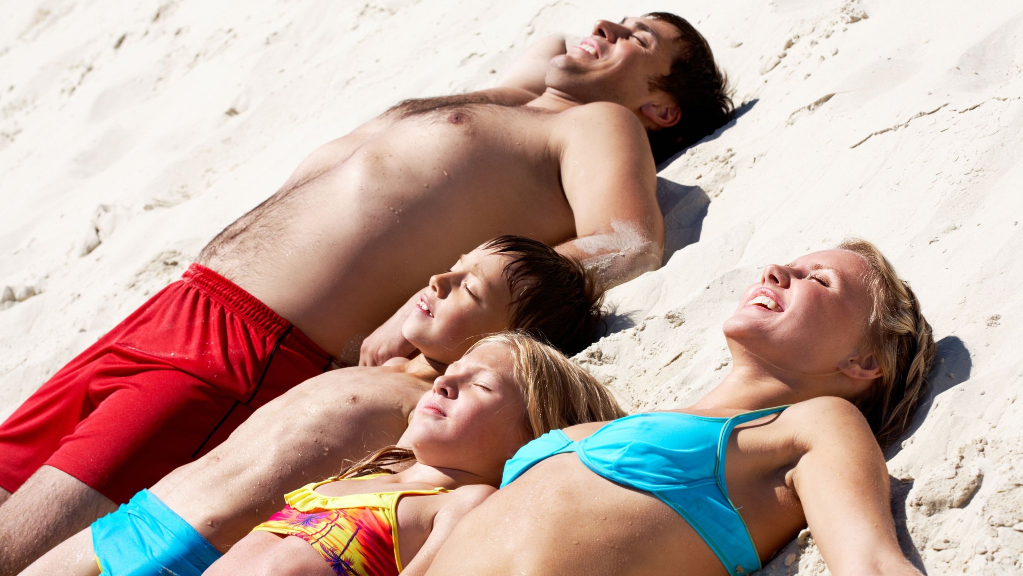 Familie mit zwei Kindern liegen in Badekleidung im Sand und sonnen sich | Bild: colourbox.de Familie mit zwei Kindern liegen in Badekleidung im Sand und sonnen sich