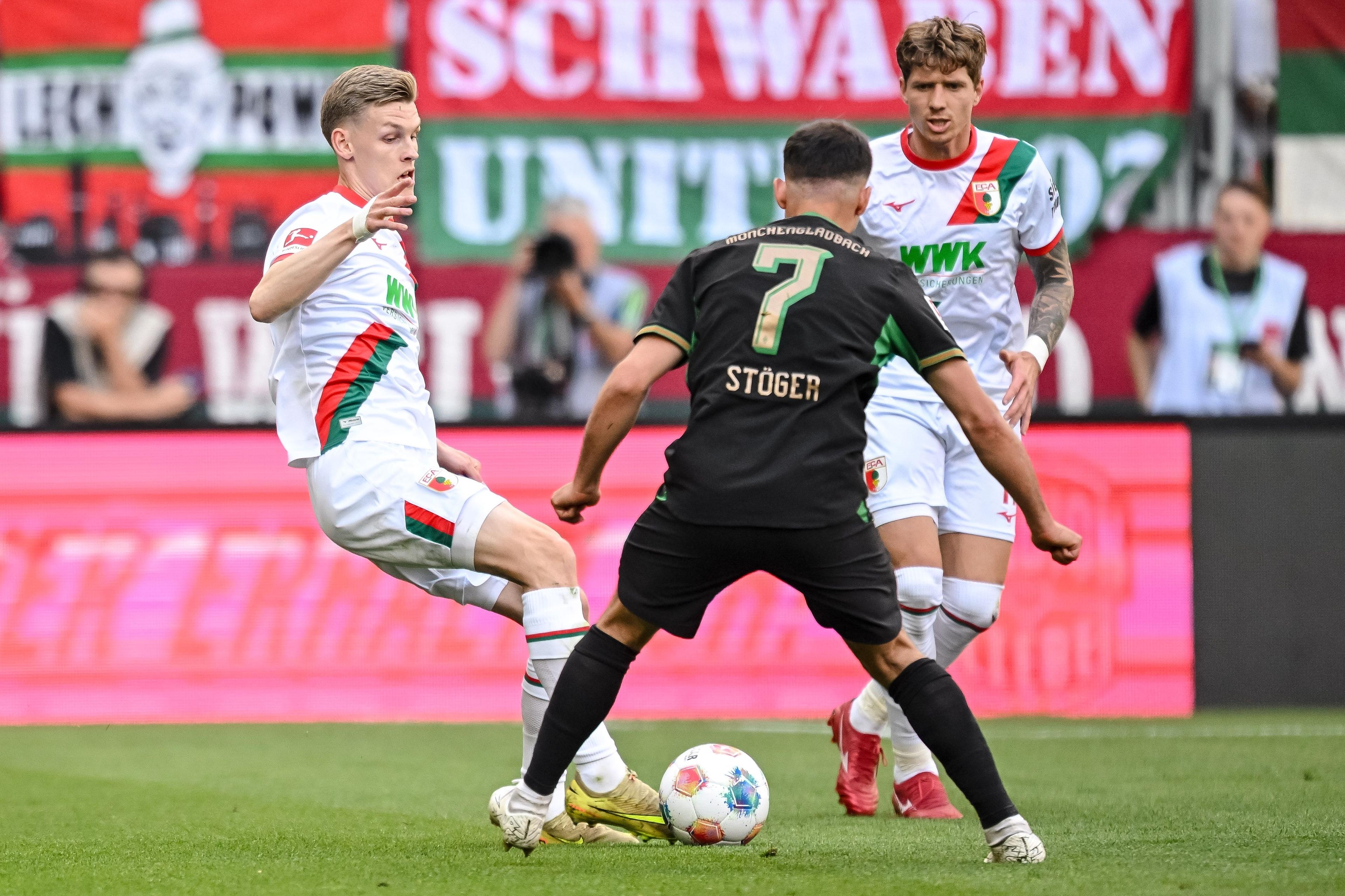 09.05.2026, Bayern, Augsburg: Fußball, Männer: Bundesliga, FC Augsburg - Borussia Mönchengladbach, 33. Spieltag, WWK-Arena. Anton Kade (l, FC Augsburg) und Kristijan Jakic (FC Augsburg) in Aktion gegen Kevin Stöger (Bor. Mönchengladbach). Foto: Harry Langer/dpa - WICHTIGER HINWEIS: Gemäß den Vorgaben der DFL Deutsche Fußball Liga bzw. des DFB Deutscher Fußball-Bund ist es untersagt, in dem Stadion und/oder vom Spiel angefertigte Fotoaufnahmen in Form von Sequenzbildern und/oder videoähnlichen Fotostrecken zu verwerten bzw. verwerten zu lassen. +++ dpa-Bildfunk +++