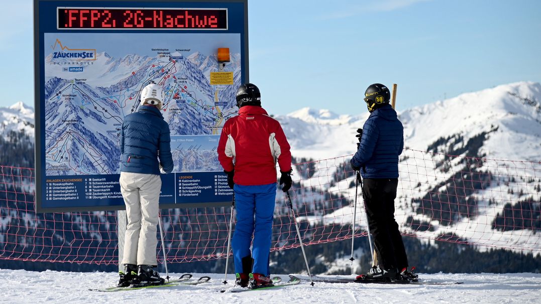 Skifahrer stehen vor einer Informationstafel mit der Aufforderung nach FFP2-Masken und 2G-Nachweis im österreichischen Skigebiet Altenmarkt-Zauchensee. 