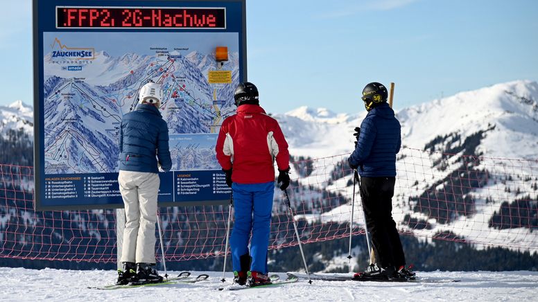 Skifahrer stehen vor einer Informationstafel mit der Aufforderung nach FFP2-Masken und 2G-Nachweis im österreichischen Skigebiet Altenmarkt-Zauchensee.  | Bild:dpa-Bildfunk/Barbara Gindl
