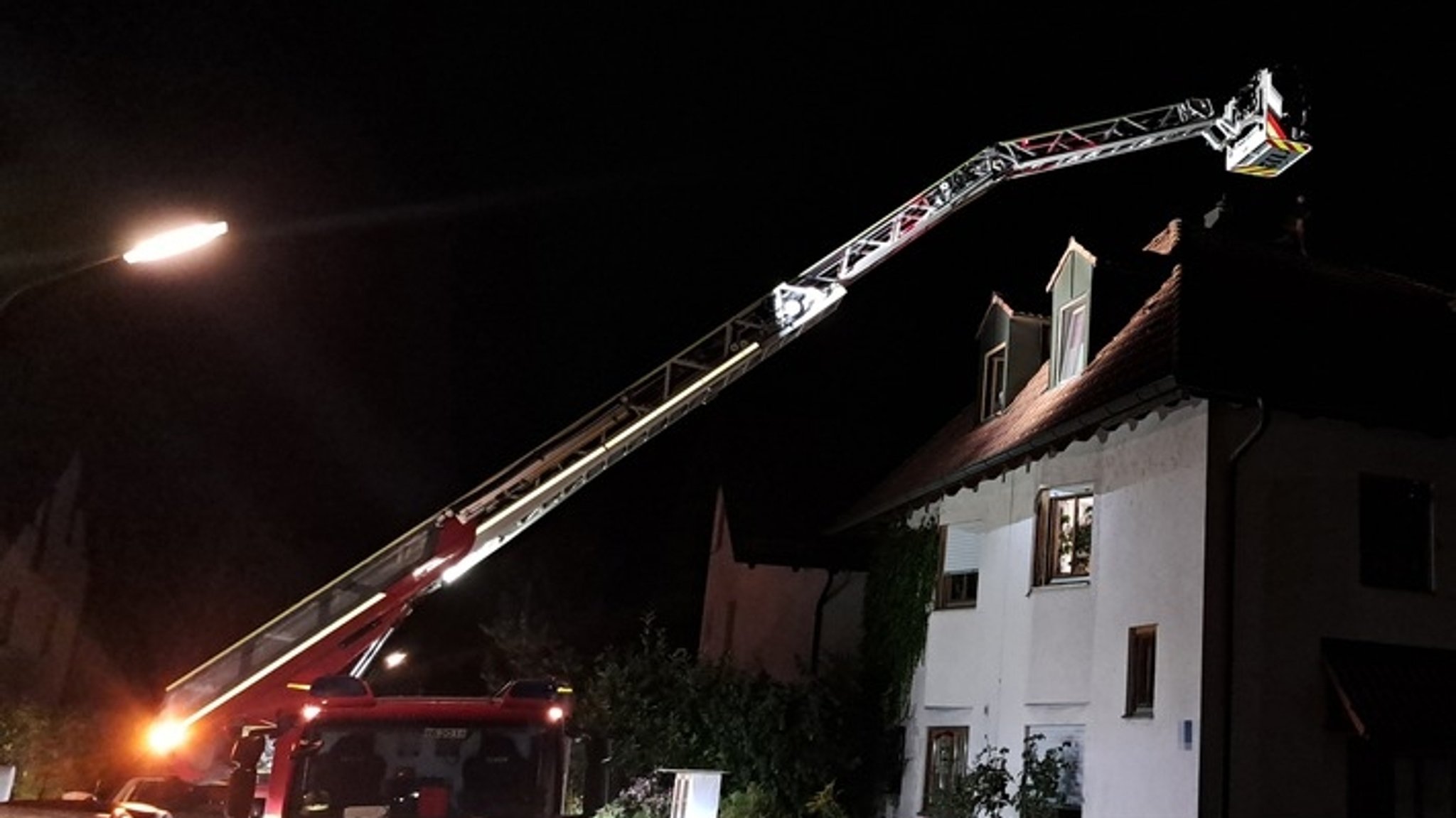 Von einem Feuerwehrauto wird eine Drehleiter ausgefahren, um einen Mann und eine Katze nachts von einem steilen Dach zu retten.