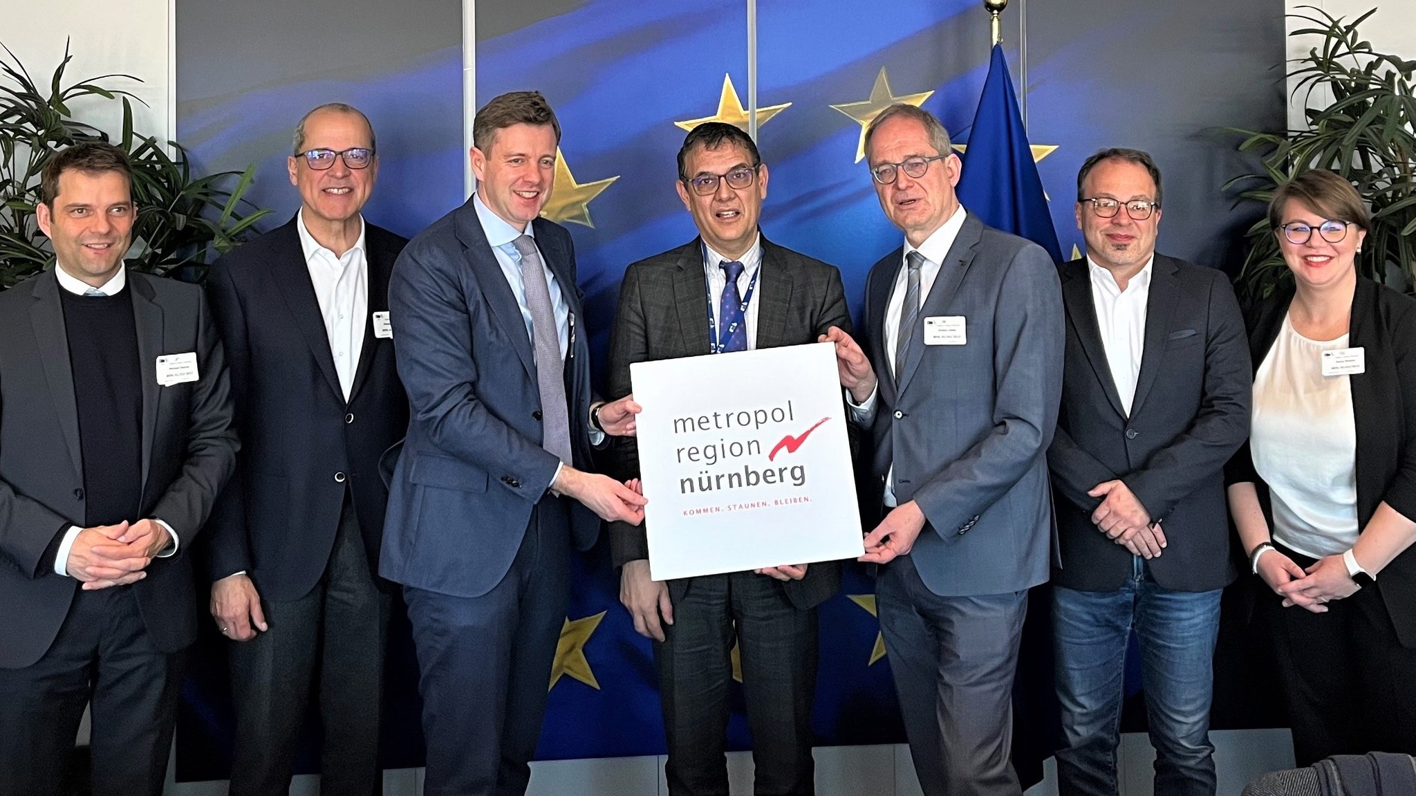 Menschen halten lachend ein Schild mit der Aufschrift "Metropolregion Nürnberg". 