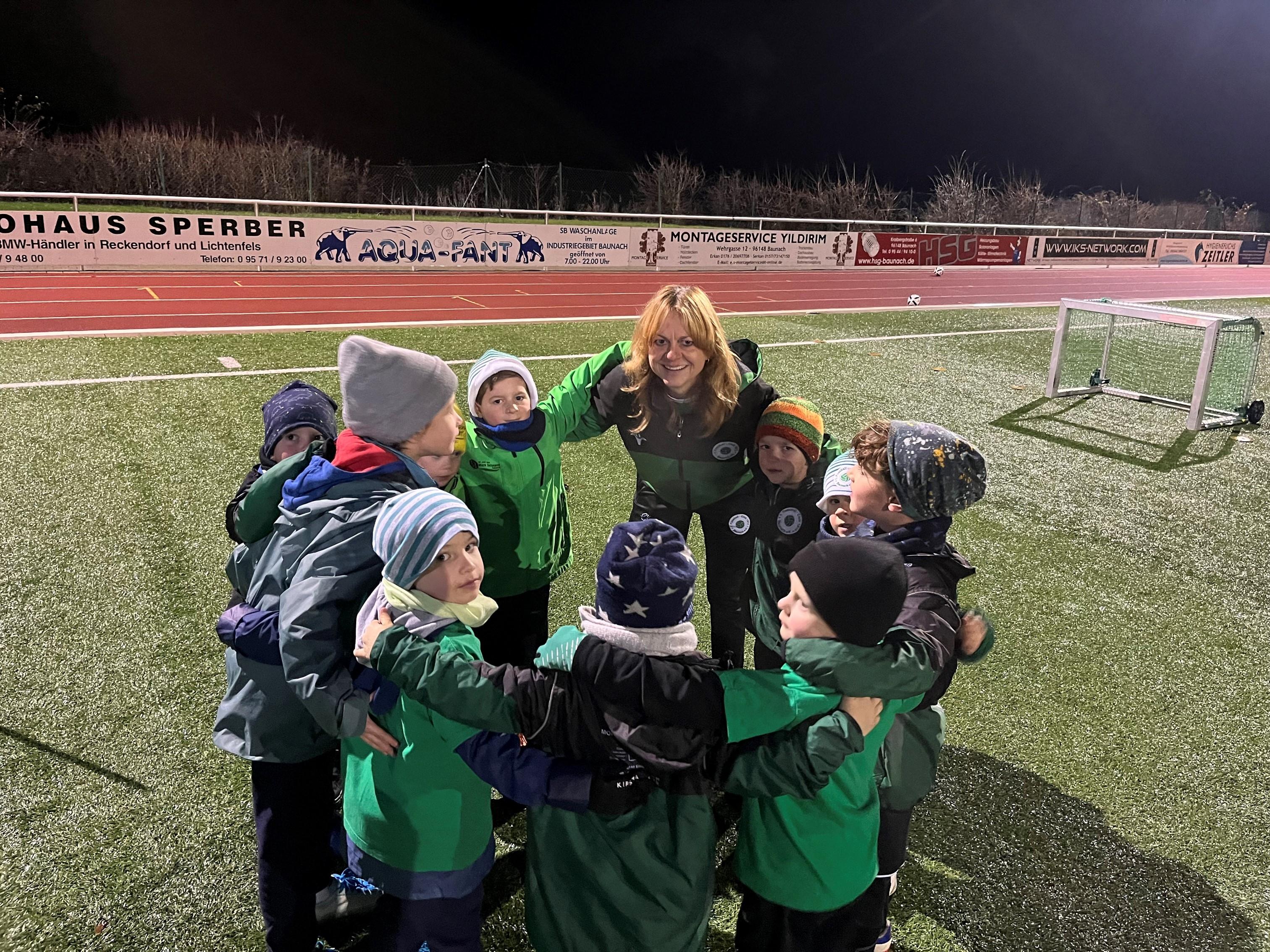 Christine Dumsky bildet mit Kindern einen Mannschaftskreis auf einem Sportplatz.