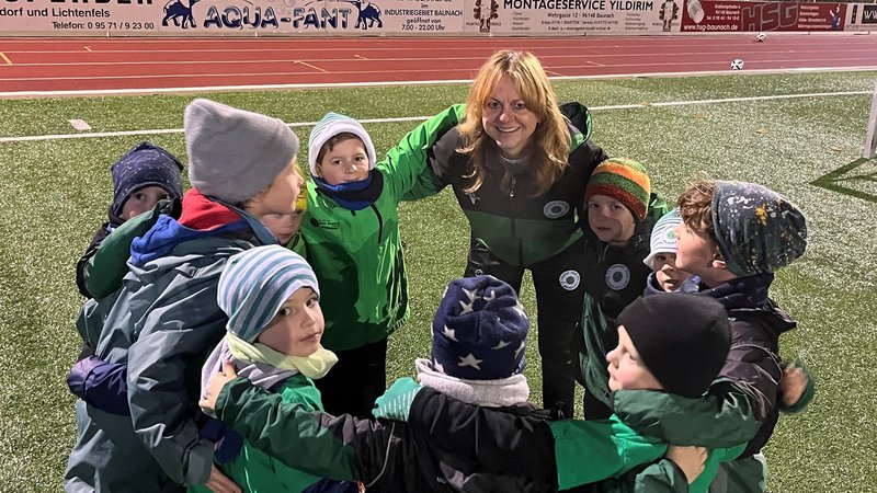 Christine Dumsky bildet mit Kindern einen Mannschaftskreis auf einem Sportplatz. | Bild: BR/Patricia Reichel Christine Dumsky bildet mit Kindern einen Mannschaftskreis auf einem Sportplatz.