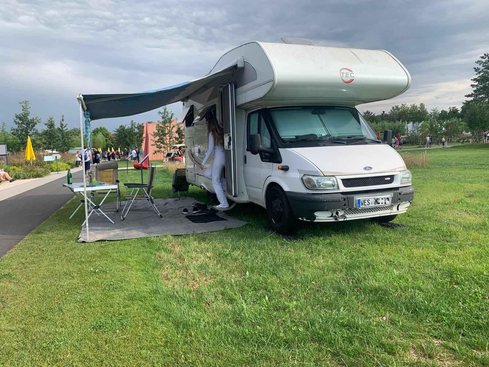 Ein Campingauto mit Tisch und Stühlen unter einem Vordach steht auf einem Rasen auf dem Gelände der Landesgartenschau bei München.