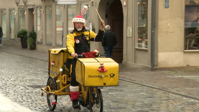 Postbote im Weihnachtsoutfit auf dem Fahrrad