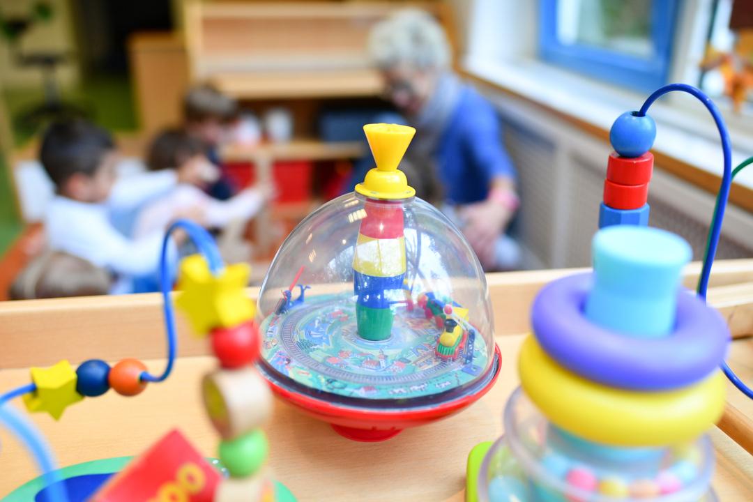 Symbolbild: Eine Erzieherin spielt in einer Kita mit Kindern. Im Vordergrund steht Spielzeug.