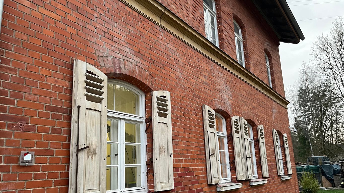 Ein rotes Backsteinhaus mit weißen Fensterläden aus Holz.
