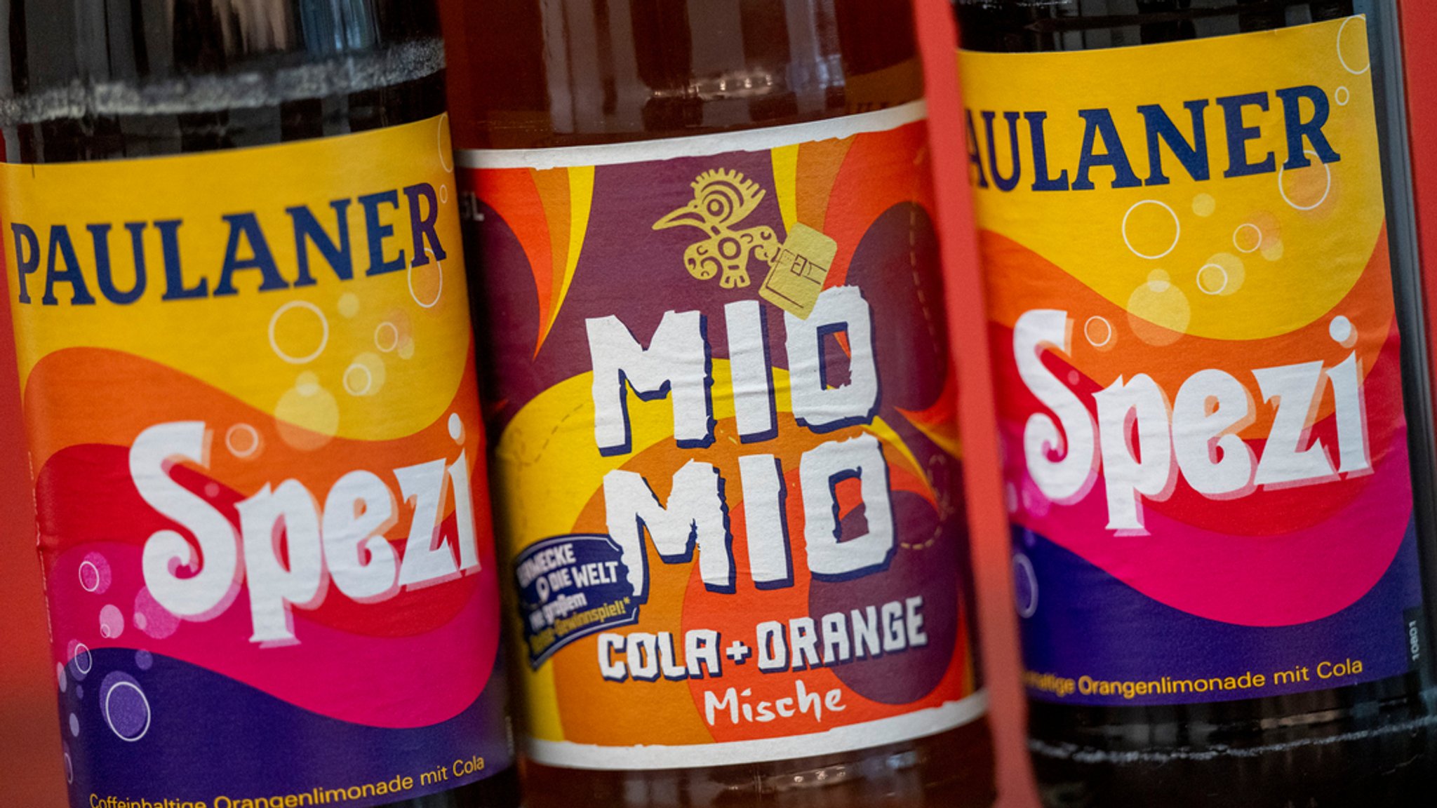 Zwei Spezi-Flaschen des Herstellers Paulaner stehen neben einer Flasche Mio-Mio-Cola-Orange-Mische (M) des Herstellers Berentzen. 