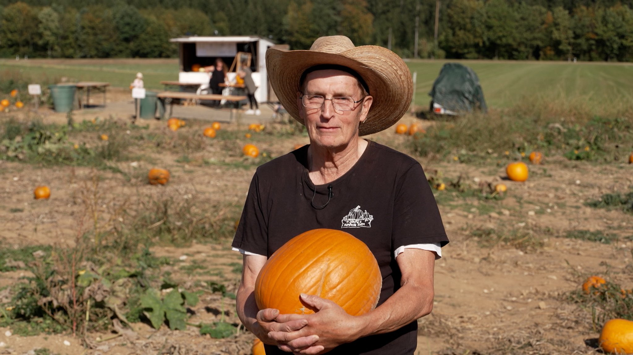 Der Amerikaner Jerry steht mit einem Kürbis im Arm auf einem Feld.