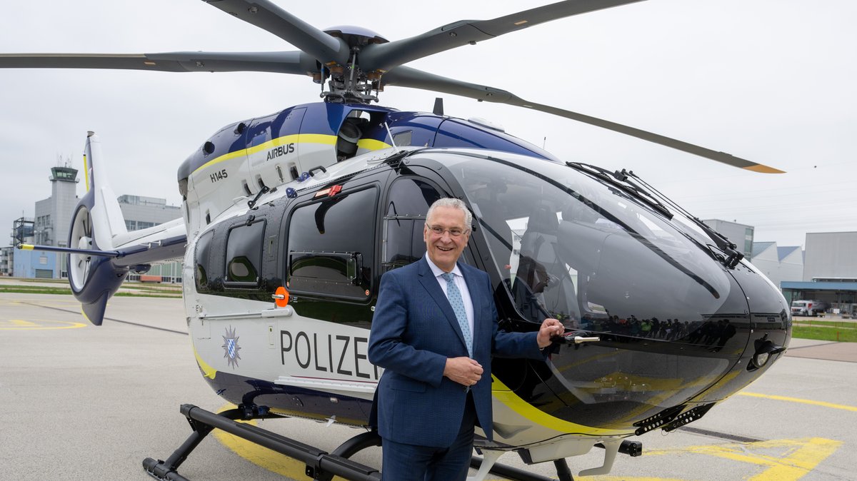 Joachim Herrmann (CSU), Innenminister von Bayern, steht neben einem Hubschrauber vom Typ Airbus H145 in der Lackierung der bayerischen Polizei. 