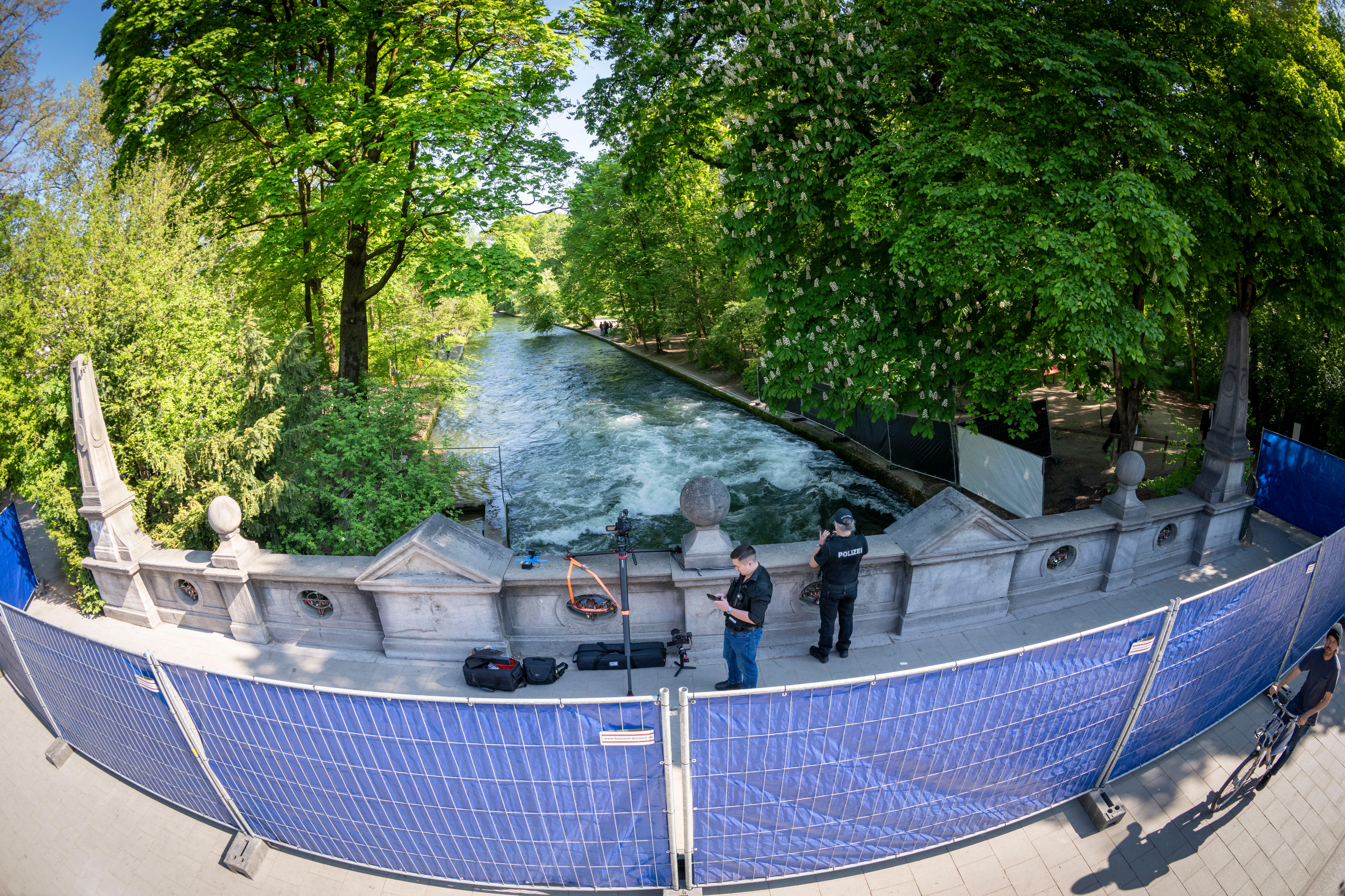 Absperrgitter mit blauen Planen gegen neugierige Blicke stehen auf einer Brücke, die über den Eisbach führt.