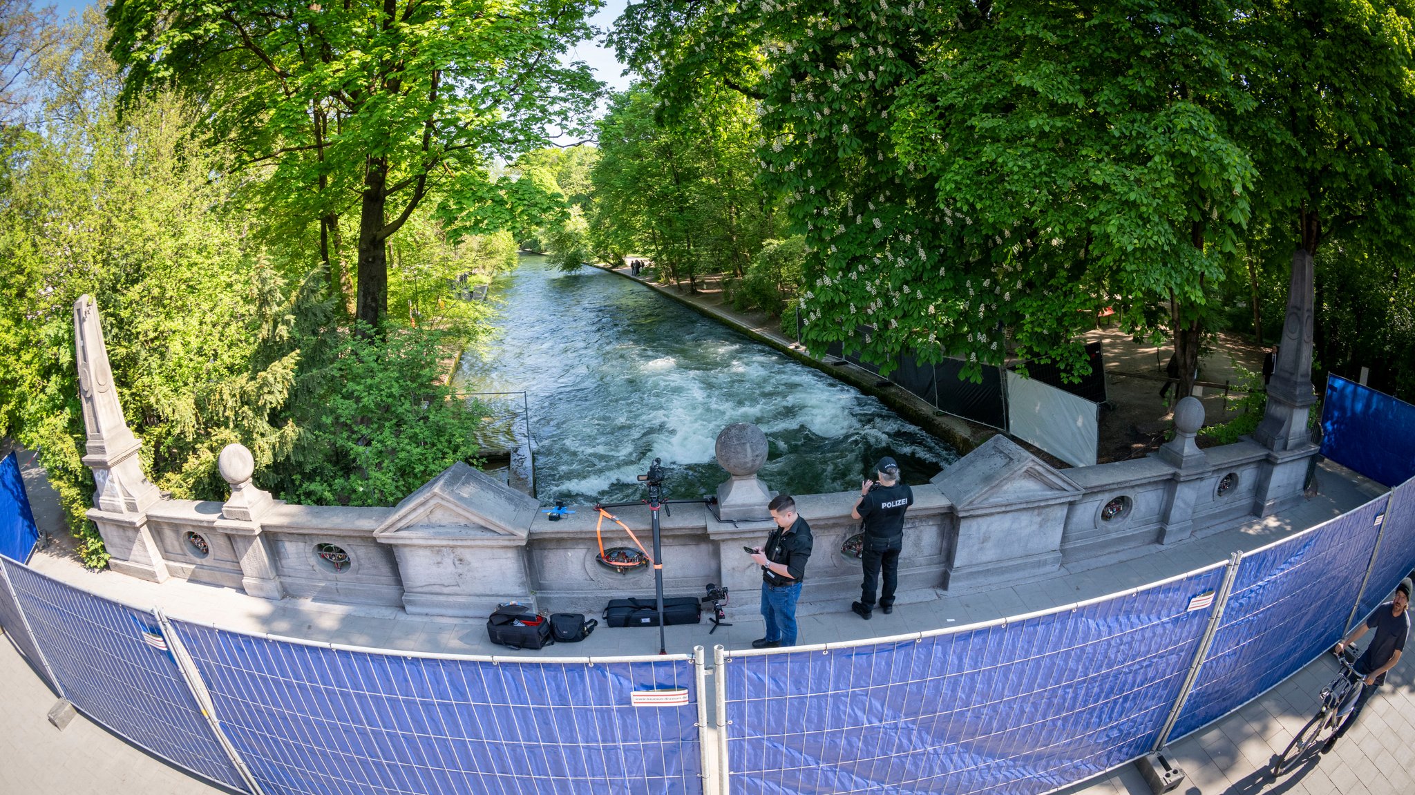 Absperrgitter mit blauen Planen gegen neugierige Blicke stehen auf einer Brücke, die über den Eisbach führt.