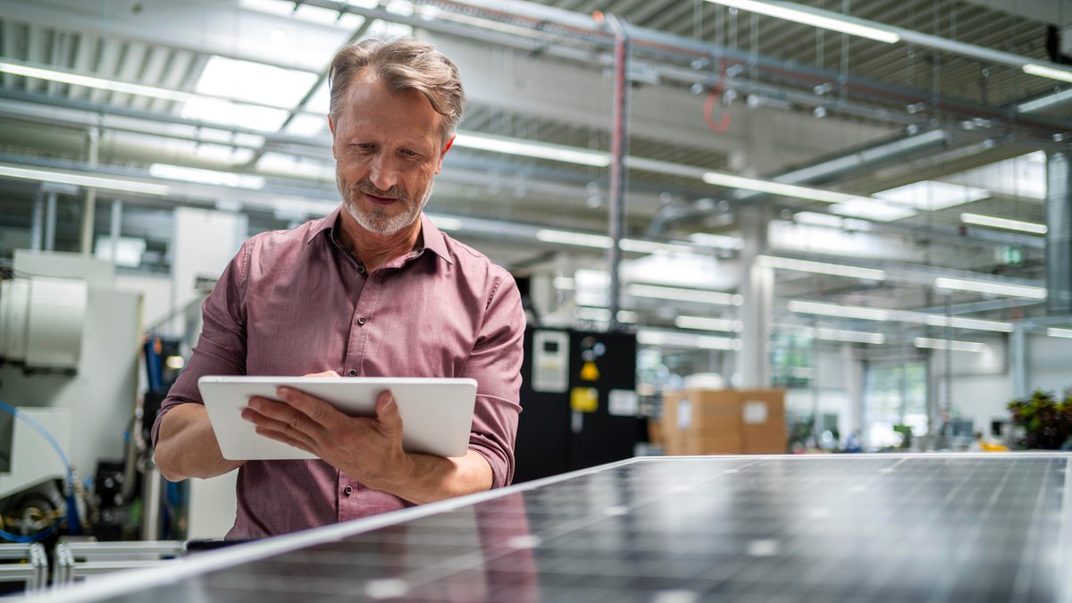 Ein älterer Mann arbeitet in einer Firma an einem Tablet, im Vordergrund ein Solarmodul (Archiv- und Symbolbild)