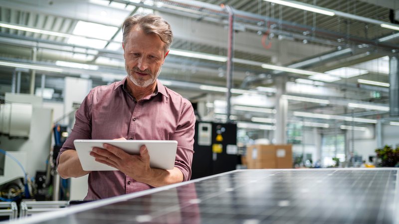 Ein älterer Mann arbeitet in einer Firma an einem Tablet, im Vordergrund ein Solarmodul (Archiv- und Symbolbild) | Bild: picture alliance / Westend61|Daniel Ingold Ein älterer Mann arbeitet in einer Firma an einem Tablet, im Vordergrund ein Solarmodul (Archiv- und Symbolbild)