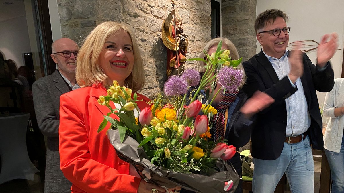 Im Landkreis Kitzingen hat sich Amtsinhaberin Tamara Bischof von den Freien Wählern deutlich durchgesetzt. Auf dem Foto hält sie einen Blumenstrauß in der Hand und steht zwischen feiernden Menschen.