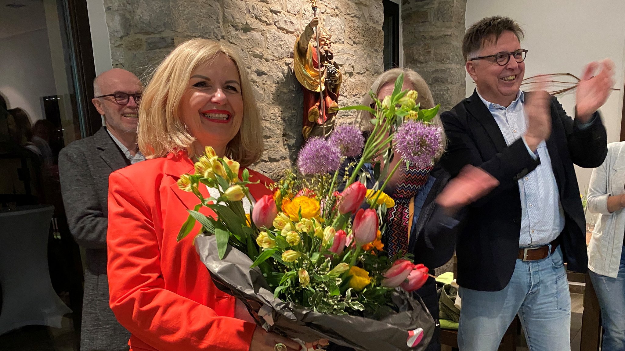 Im Landkreis Kitzingen hat sich Amtsinhaberin Tamara Bischof von den Freien Wählern deutlich durchgesetzt. Auf dem Foto hält sie einen Blumenstrauß in der Hand und steht zwischen feiernden Menschen. | Bild: BR/Markus Klingele Im Landkreis Kitzingen hat sich Amtsinhaberin Tamara Bischof von den Freien Wählern deutlich durchgesetzt. Auf dem Foto hält sie einen Blumenstrauß in der Hand und steht zwischen feiernden Menschen.