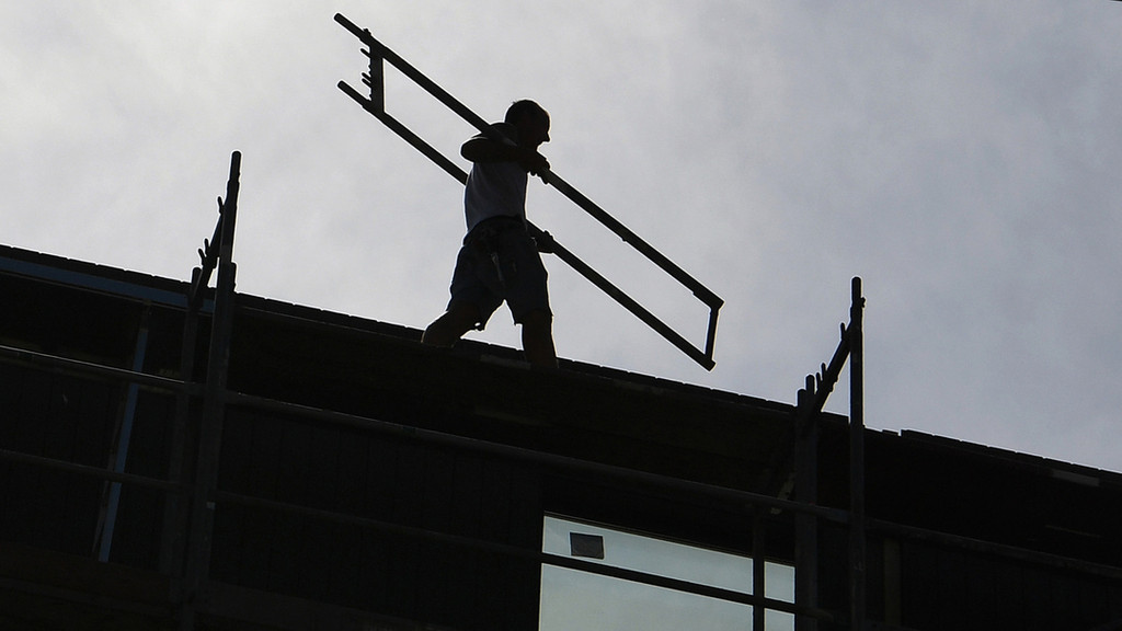 Ein Arbeiter trägt auf einer Baustelle ein Teil eines Baugerüsts