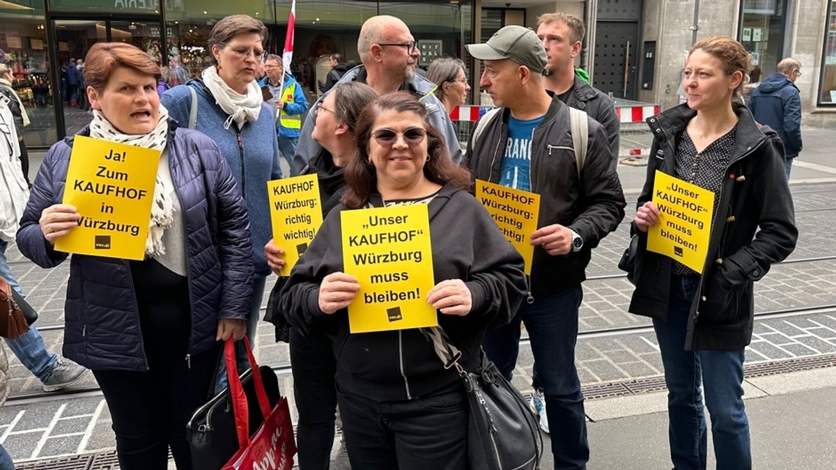 Menschen halten ein je ein gelbes Plakat mit der Aufschrift "Unser Kaufhof Würzburg muss bleiben!"