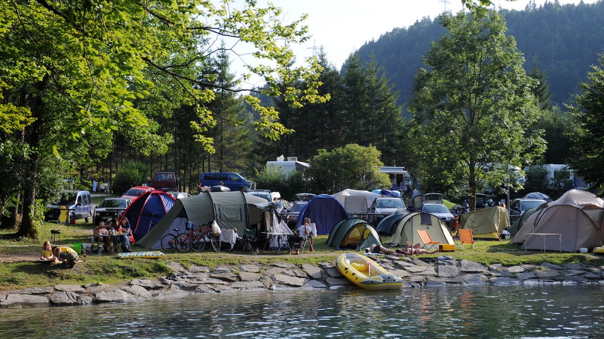 Zelte und Schlauchboote stehen am Walchensee auf einem Campingplatz am Seeufer.
