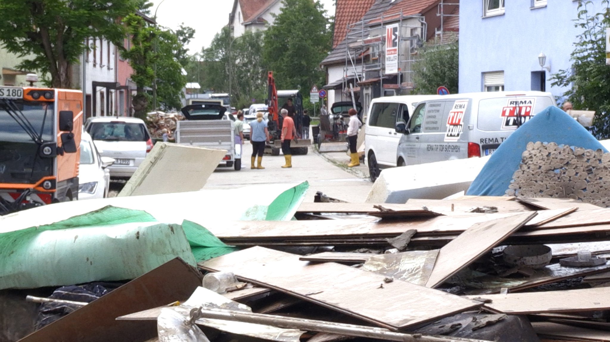 In Günzburg stehen Anwohner in Gummistiefeln auf der Straße, für die Sperrmüll-Abholung aufgetürmt liegen um sie herum Dinge, die vom Hochwasser zerstört wurden.