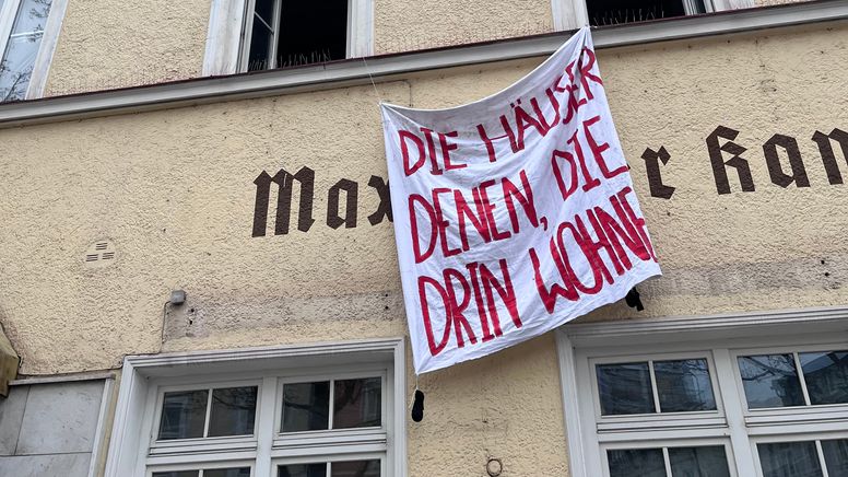 Zu sehen ist ein Transparent, auf dem "Die Häuser denen, die drin wohnen" steht.  | Bild:BR/Dagmar Bohrer-Glas
