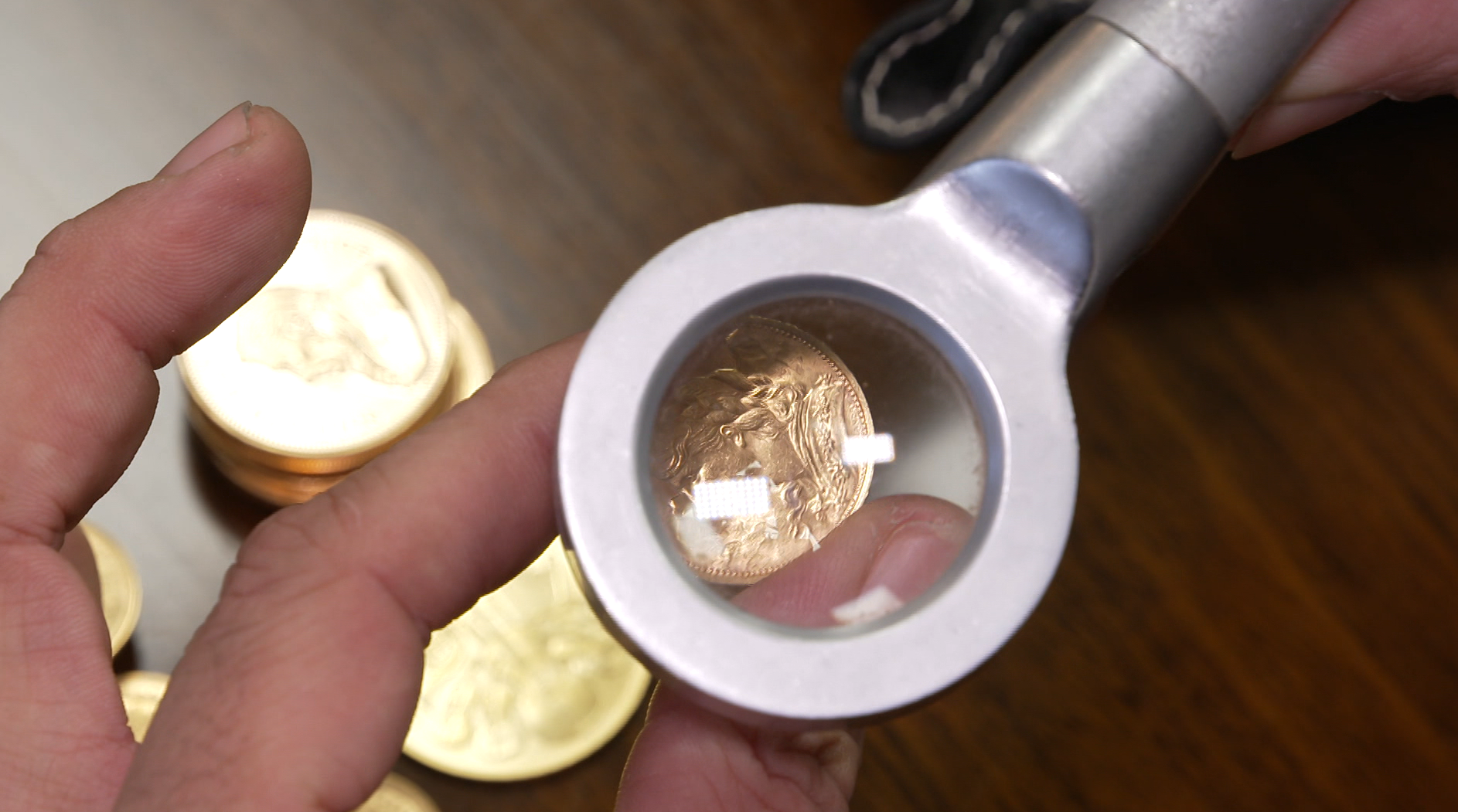 (Symbolbild) Goldmünzen unter der Lupe.