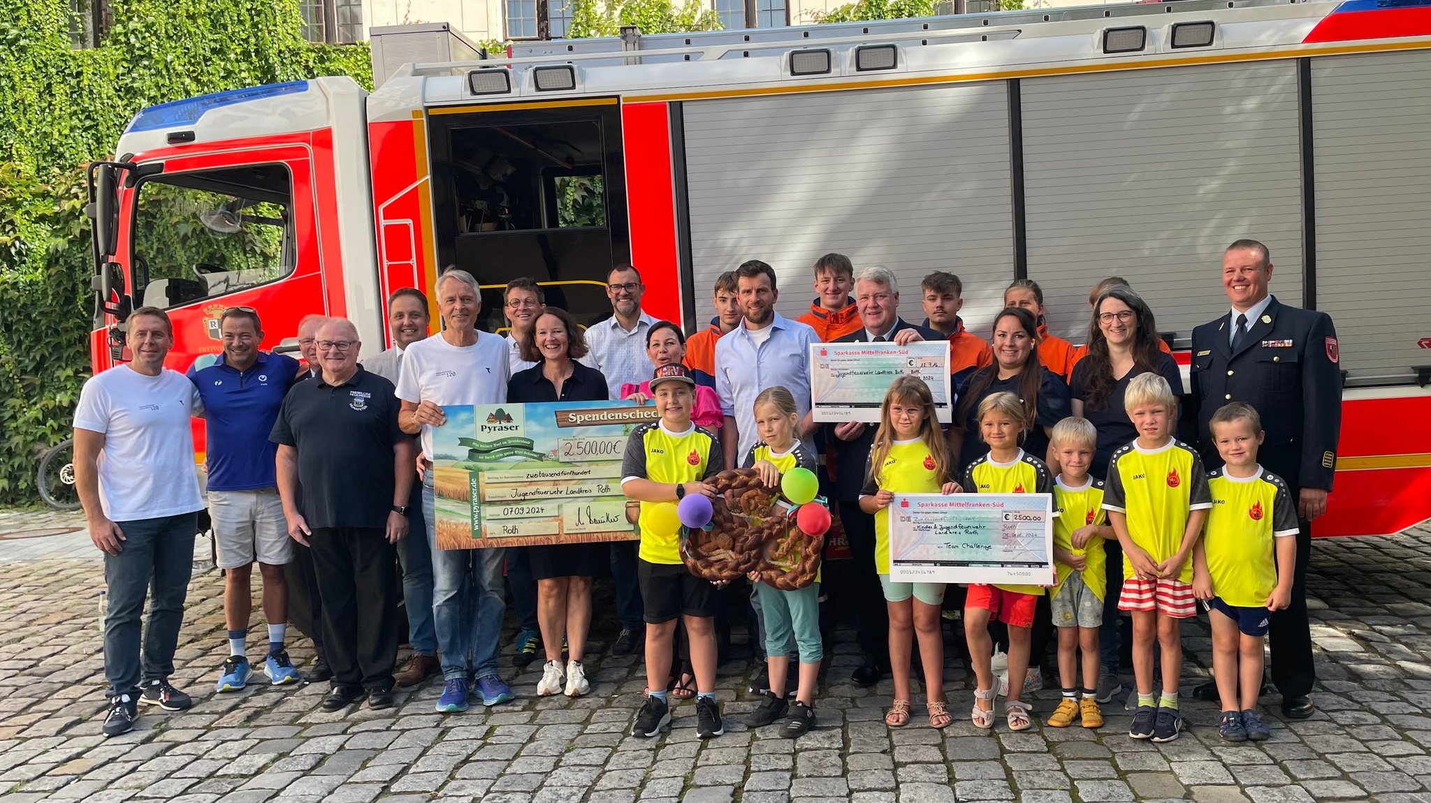 Jonas Deichmann, sein Team, die Feuerwehr und Politiker stehen vor einem Feuerwehrauto. 