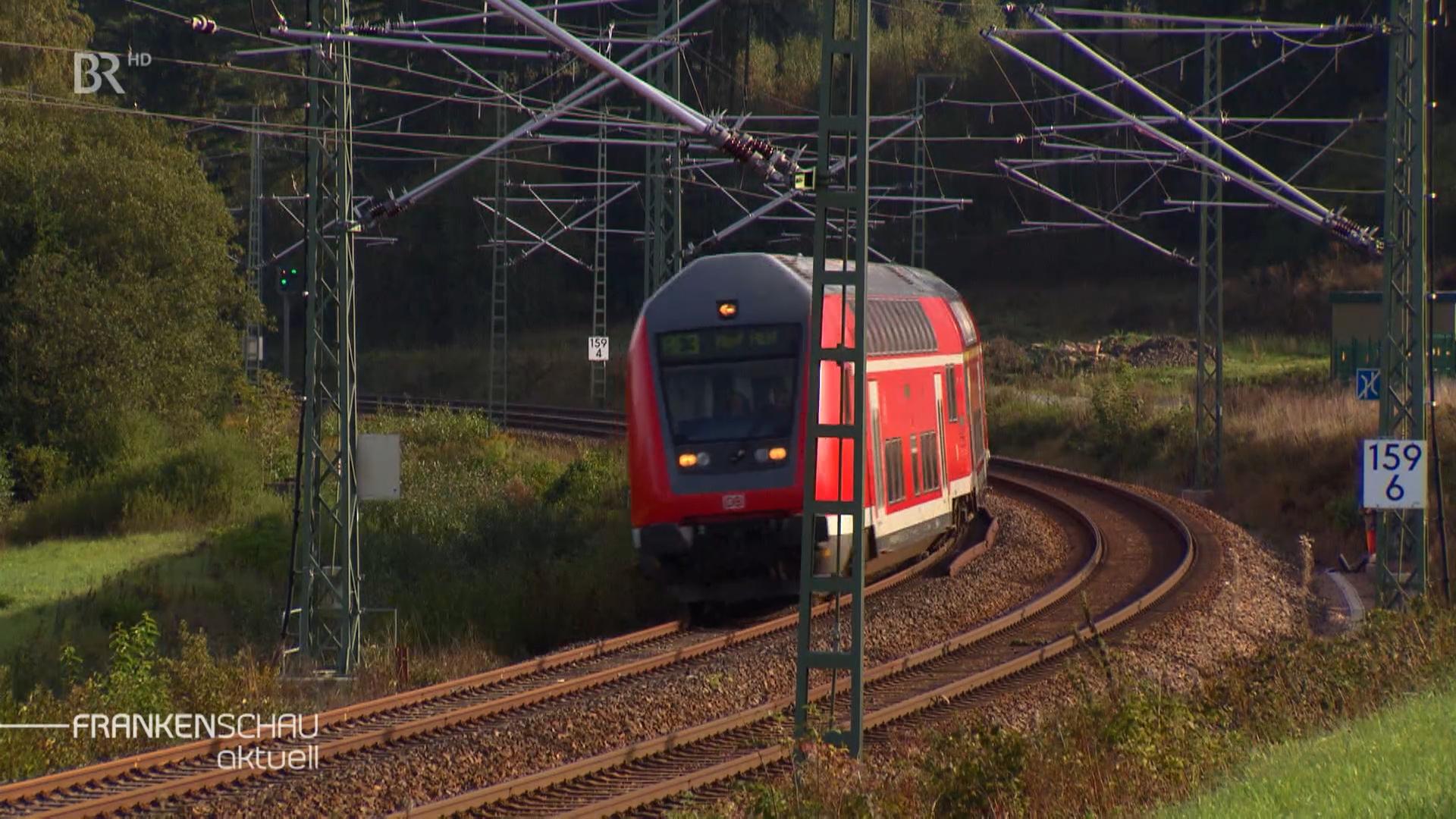 Ein roter Zug fährt, im Hintergrund Wald. 